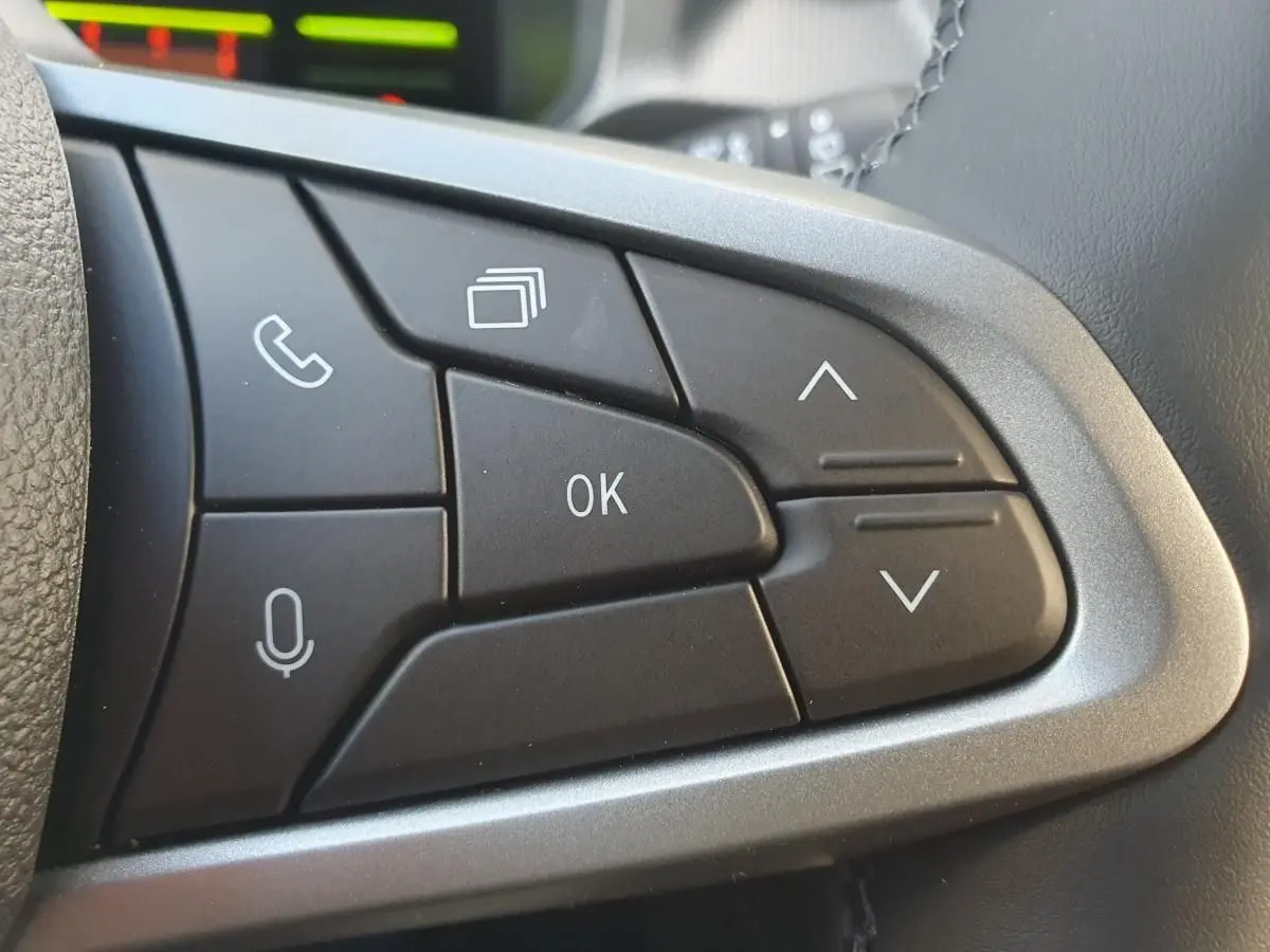 Gros plan sur les commandes multifonctions noires du volant du Dacia Duster 2026, finition métal brossé.