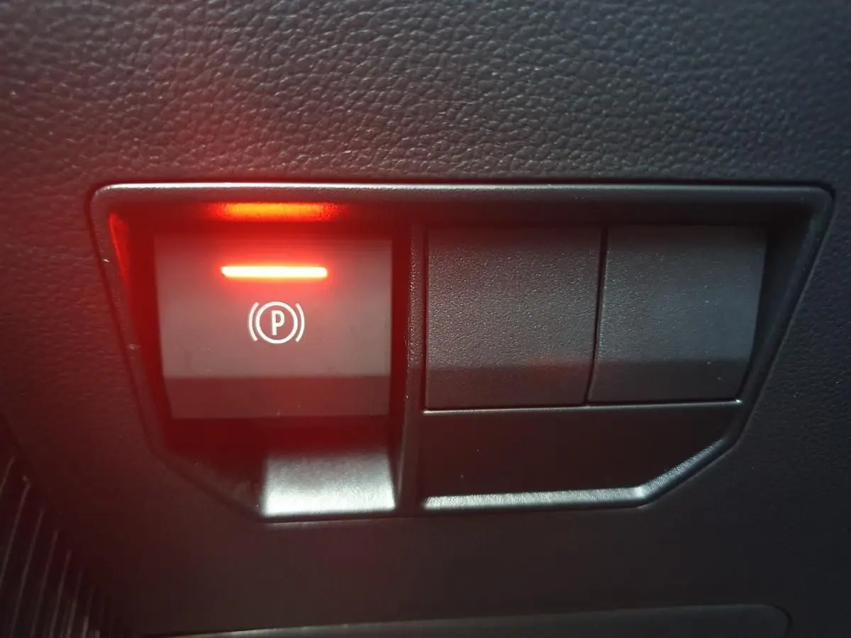 Gros plan sur le bouton de frein de stationnement électrique allumé, intérieur noir du Dacia Duster 2026.