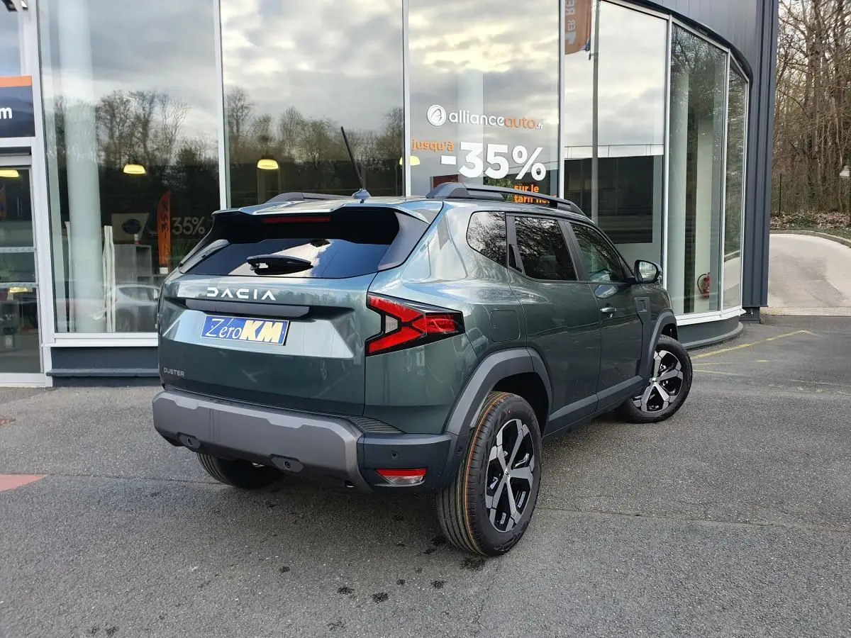 Vue 3/4 arrière droite du Dacia Duster vert cèdre 2026 avec jantes alliage 18” diamantées et barres de toit.
