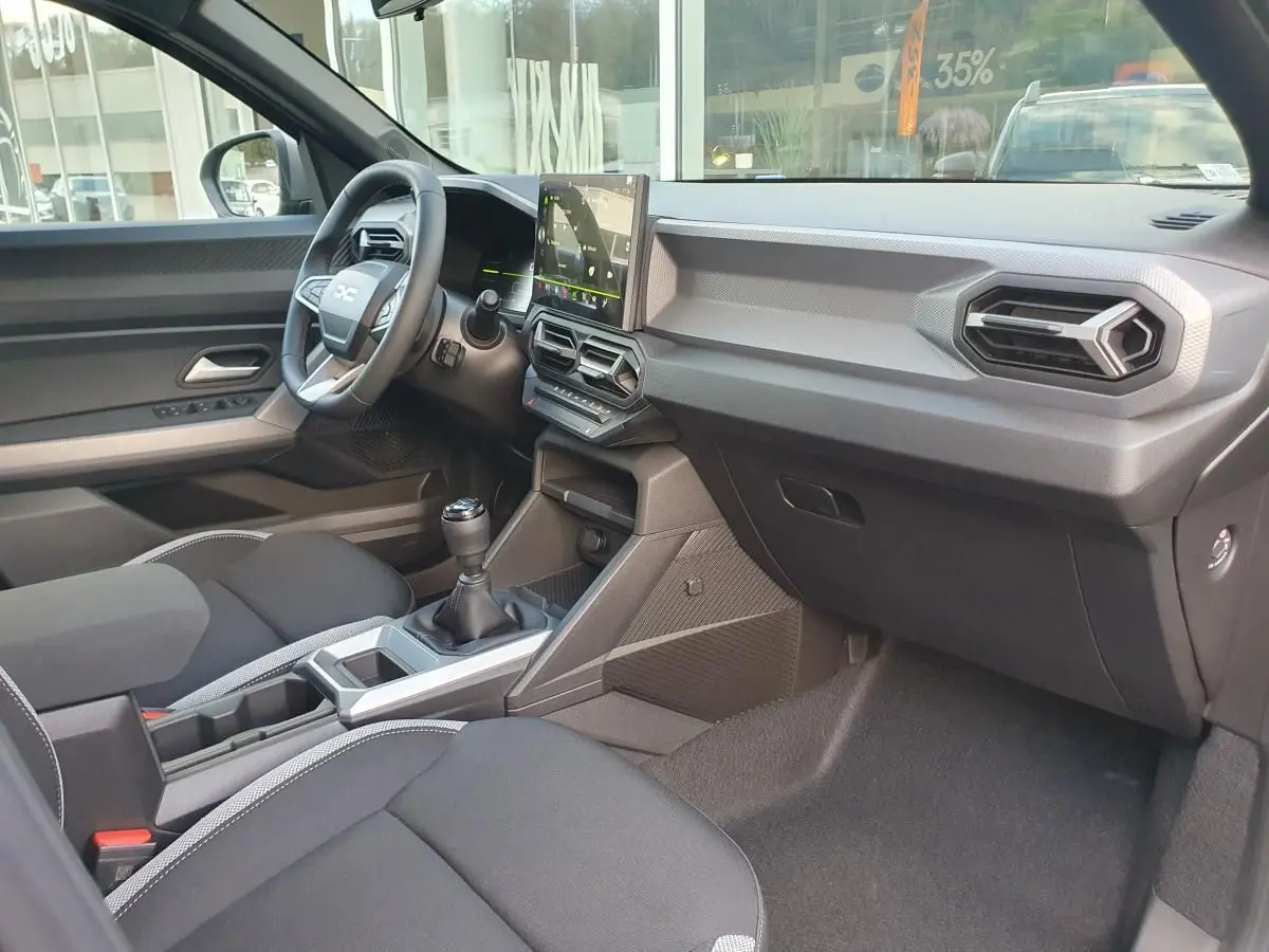 Vue intérieure côté passager du Dacia Duster 2026, montrant la console centrale avec boîte manuelle et écran tactile.