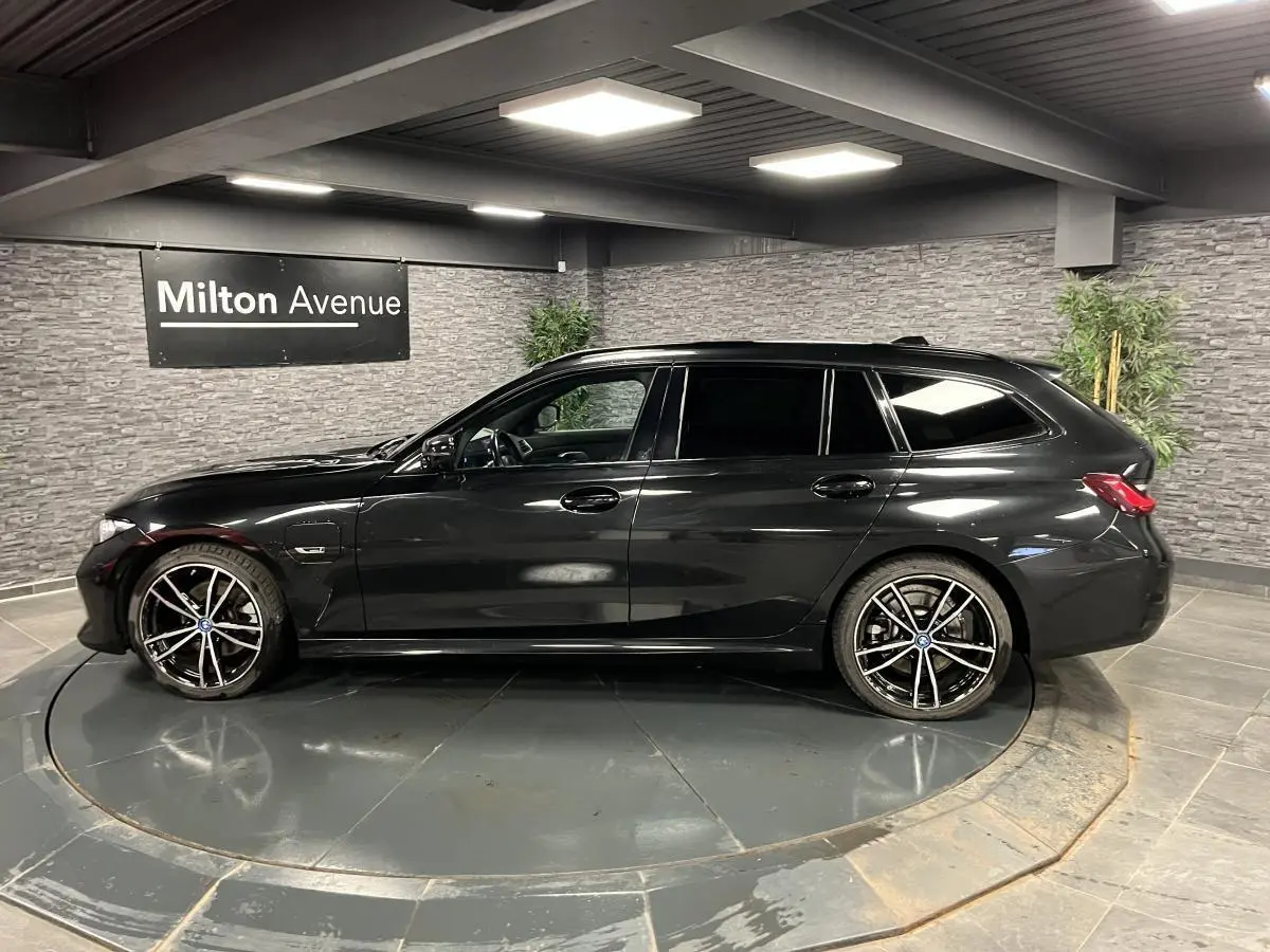 BMW Série 3 320e Touring noire vue de profil côté gauche avec jantes 19 pouces bicolores en intérieur showroom.