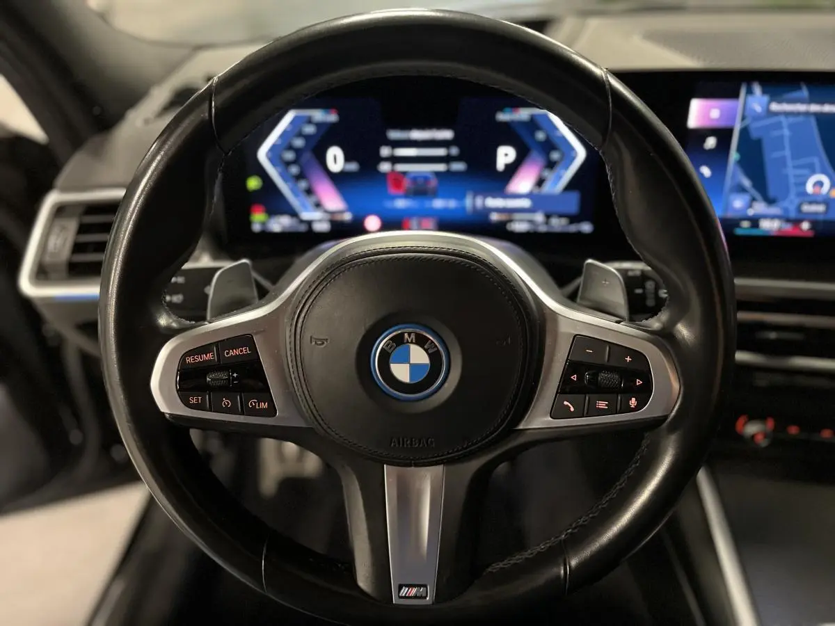 Vue rapprochée du volant M en cuir noir avec commandes intégrées et tableau de bord numérique lumineux d'une BMW Série 3 Touring.