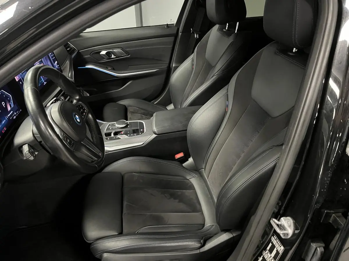 Vue intérieure côté conducteur de la BMW Série 3 320e Touring noire, sièges sport M en cuir et alcantara avec surpiqûres bleues.