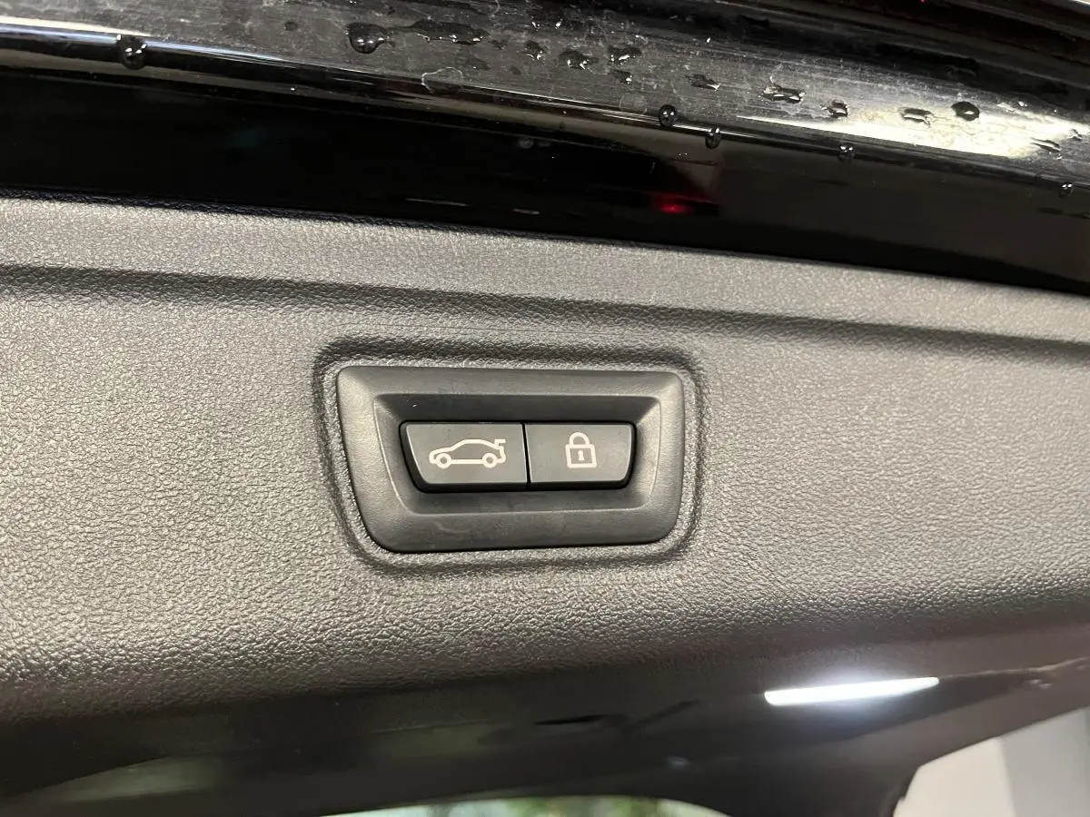 Gros plan sur les boutons d’ouverture et de verrouillage du coffre d’une BMW Série 3 Touring noire, vue intérieure du hayon.