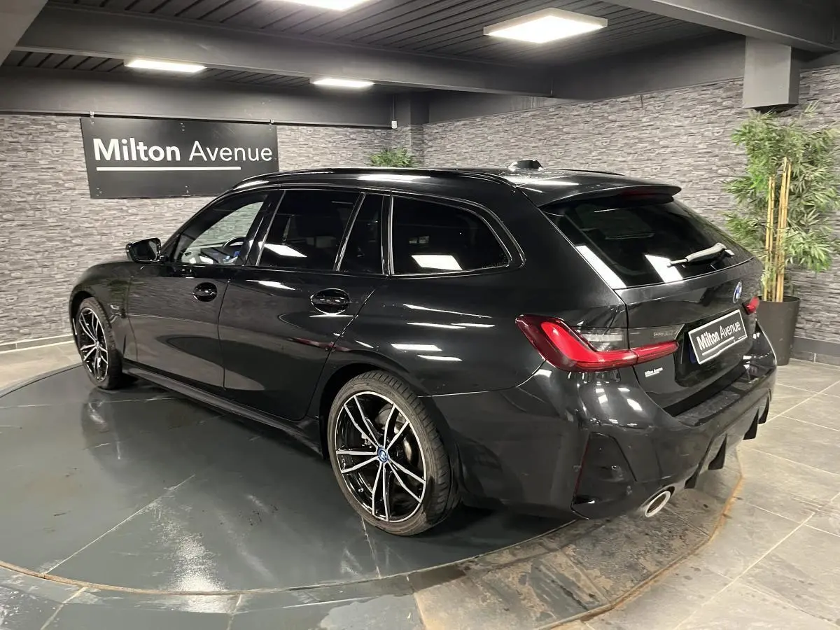 BMW Série 3 320e Touring noire vue 3/4 arrière droit, jantes M sport 19 pouces et double sortie d’échappement.