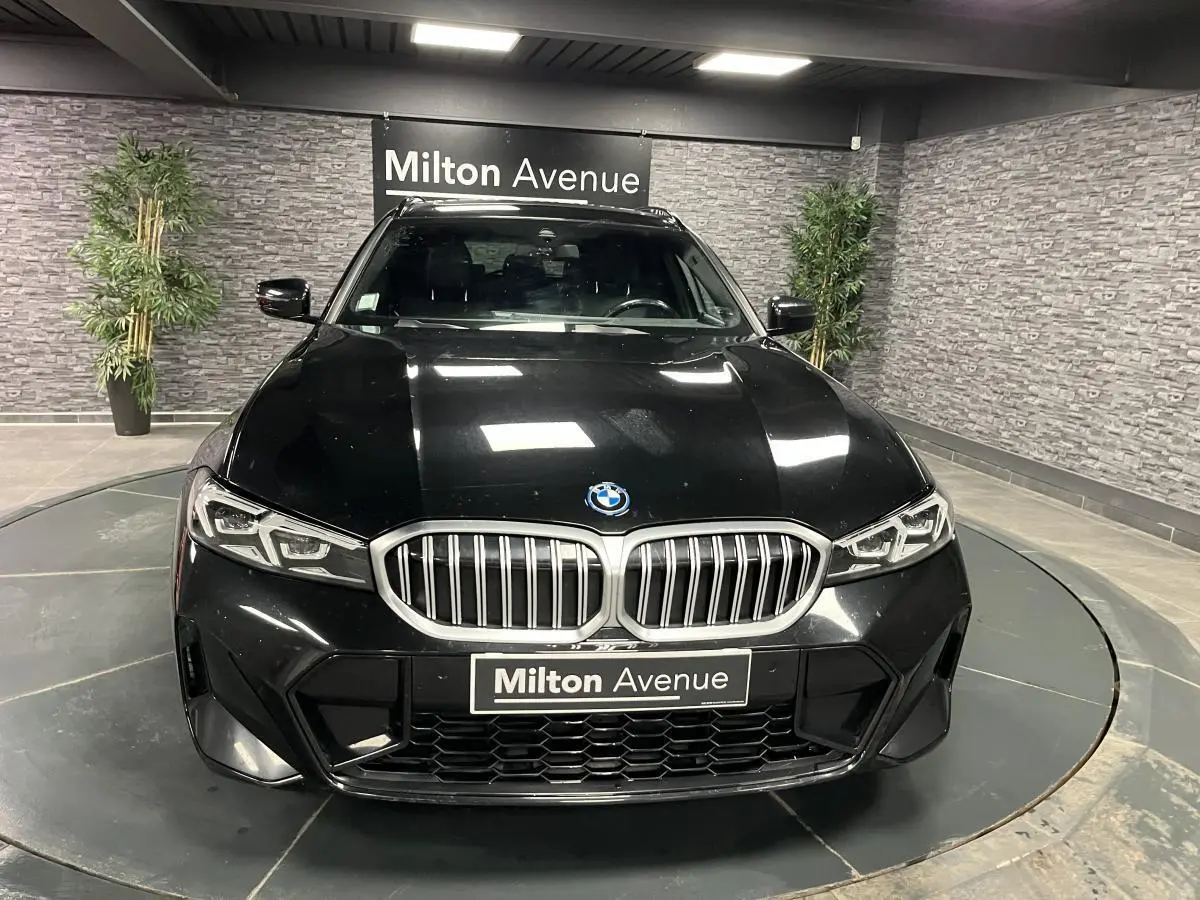Vue avant d'une BMW Série 3 G21 320e Touring noire avec calandre double haricot et phares LED, en showroom.