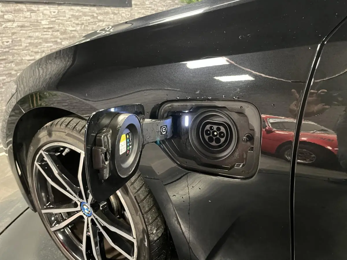 Prise de recharge ouverte côté gauche arrière d’une BMW Série 3 Touring 320e noire avec jante 19 pouces bicolore.
