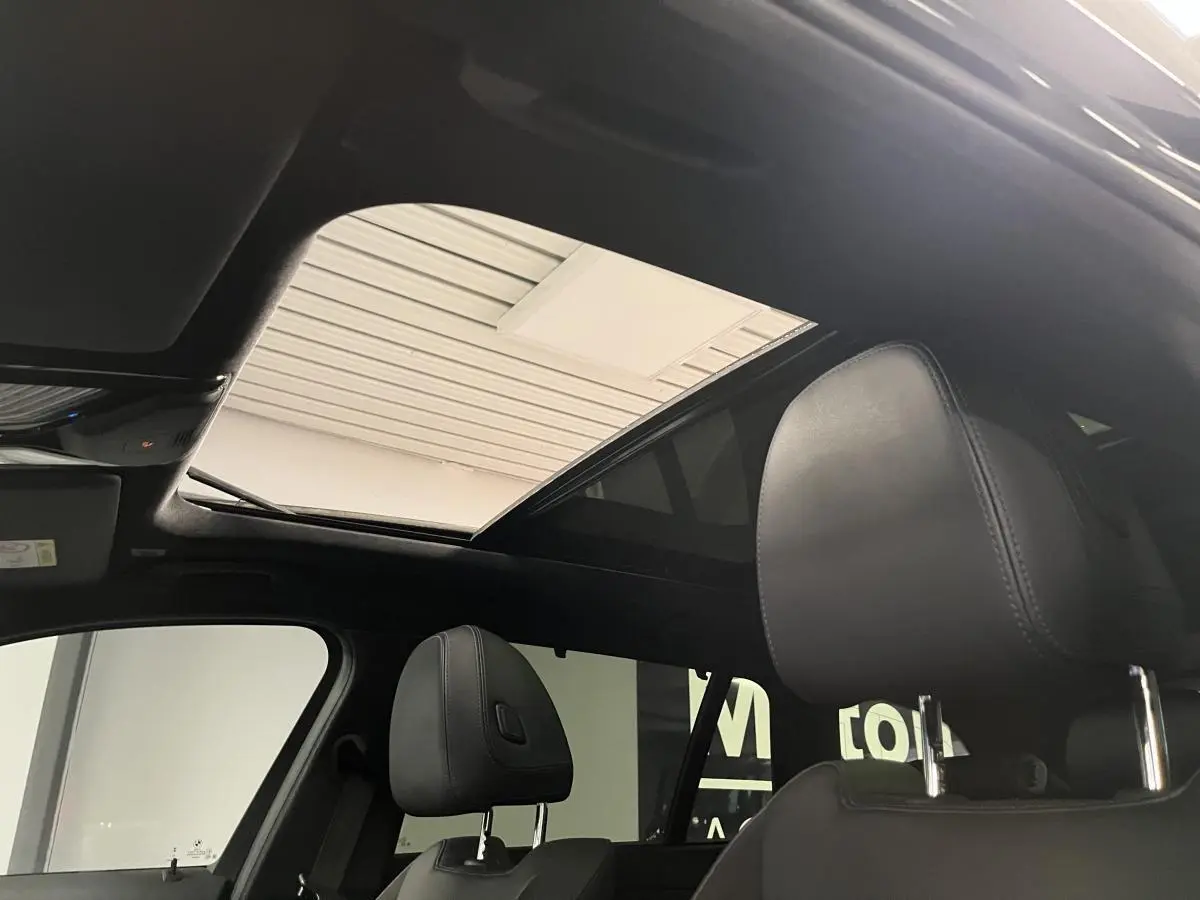 Vue intérieure du toit ouvrant panoramique en verre et des appuis-tête avant en cuir noir d'une BMW Série 3 Touring noire.