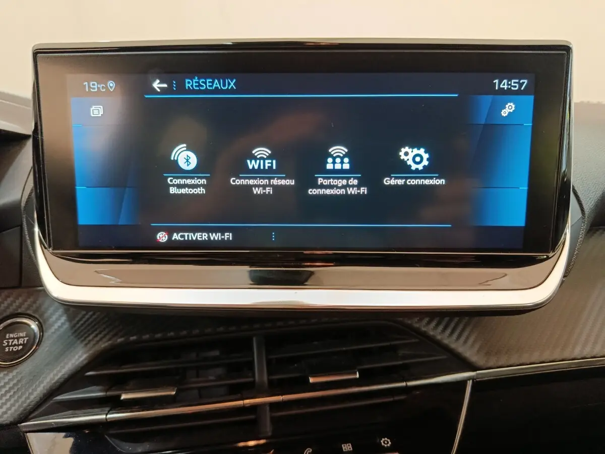 Vue rapprochée de l'écran tactile central affichant les options de connexion réseau dans l'habitacle noir d'une Peugeot 208 blanche.