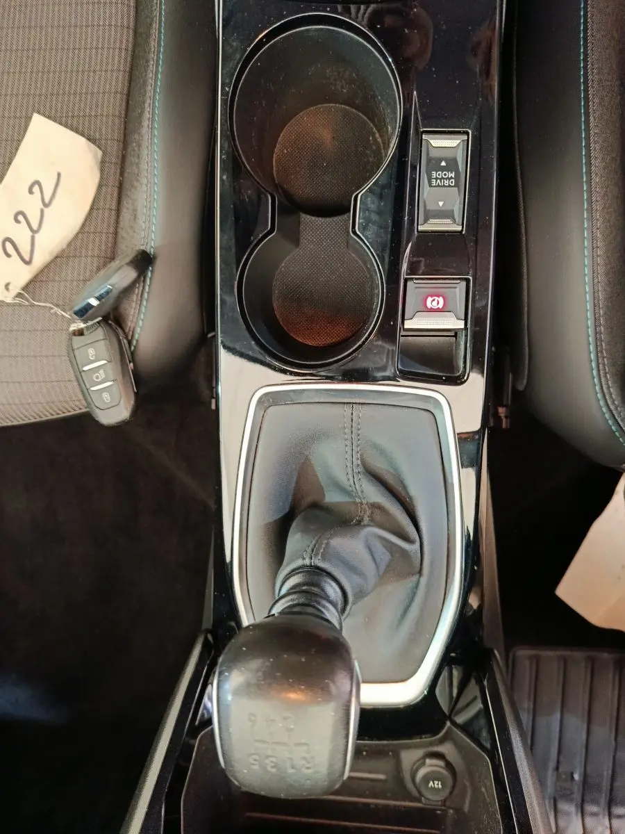 Vue plongeante sur la console centrale noire de la Peugeot 208 blanche, avec levier de vitesse manuel et porte-gobelets.
