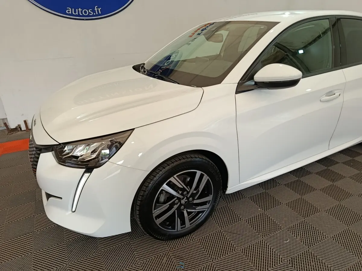 Vue 3/4 avant droit d’une Peugeot 208 blanche avec phares LED et jantes alliage noires.