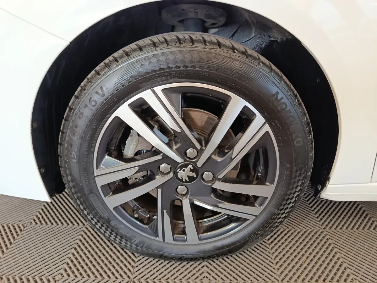 Gros plan sur la roue avant gauche de la Peugeot 208 blanche, mettant en valeur la jante alliage au design moderne.