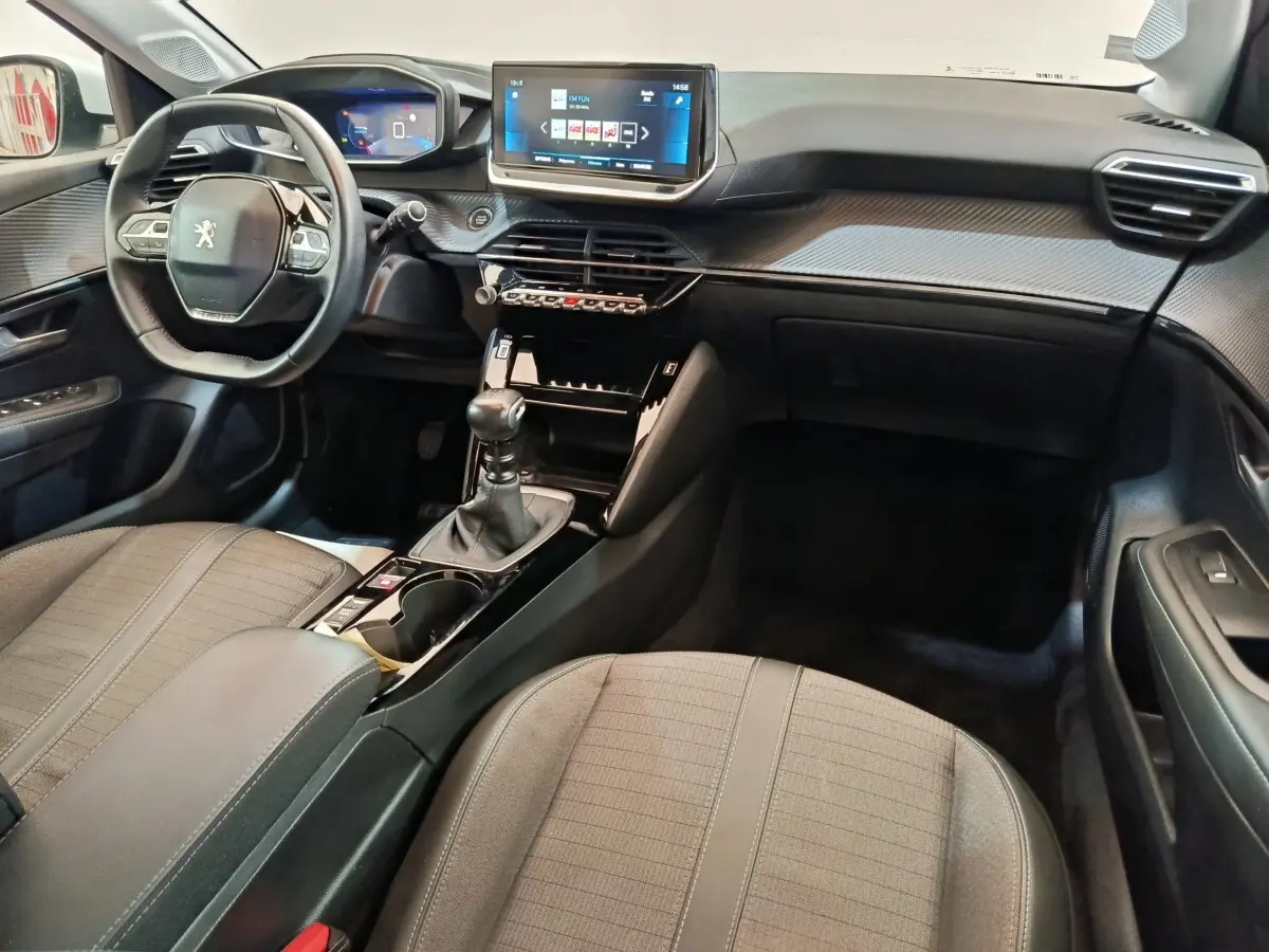 Intérieur avant droit de la Peugeot 208 PureTech 100 blanc, tableau de bord avec écran tactile 10 pouces et boîte manuelle.