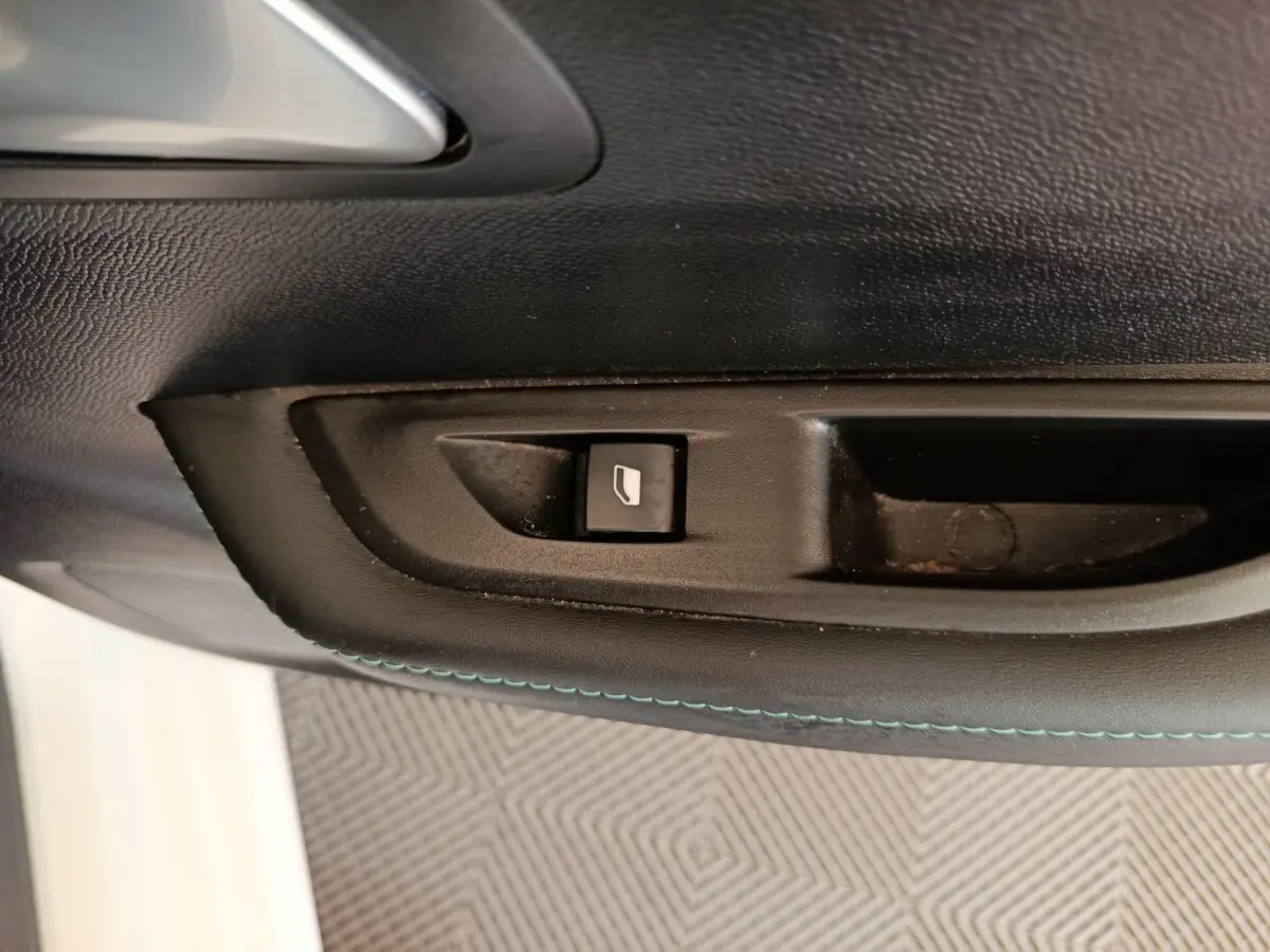 Gros plan sur le bouton de commande de la vitre côté conducteur, intérieur noir avec surpiqûres bleues, Peugeot 208 blanc.