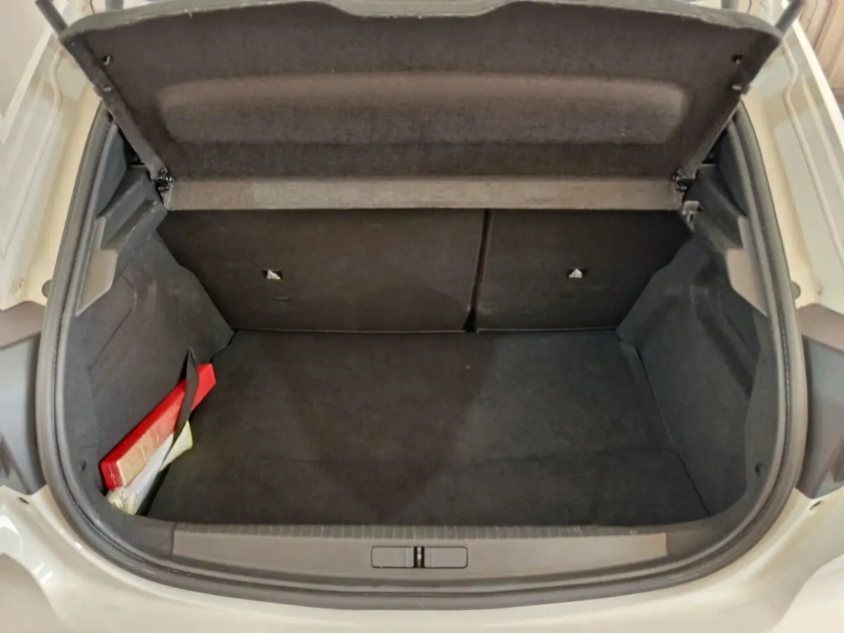 Coffre ouvert vu de face d’une Peugeot 208 blanche, intérieur noir avec un kit de sécurité rouge à gauche.