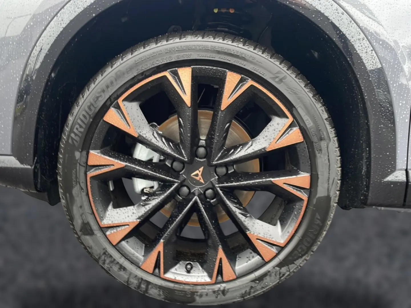 Gros plan sur la jante noire et cuivre du CUPRA Formentor gris graphene, avec pneus Bridgestone mouillés.