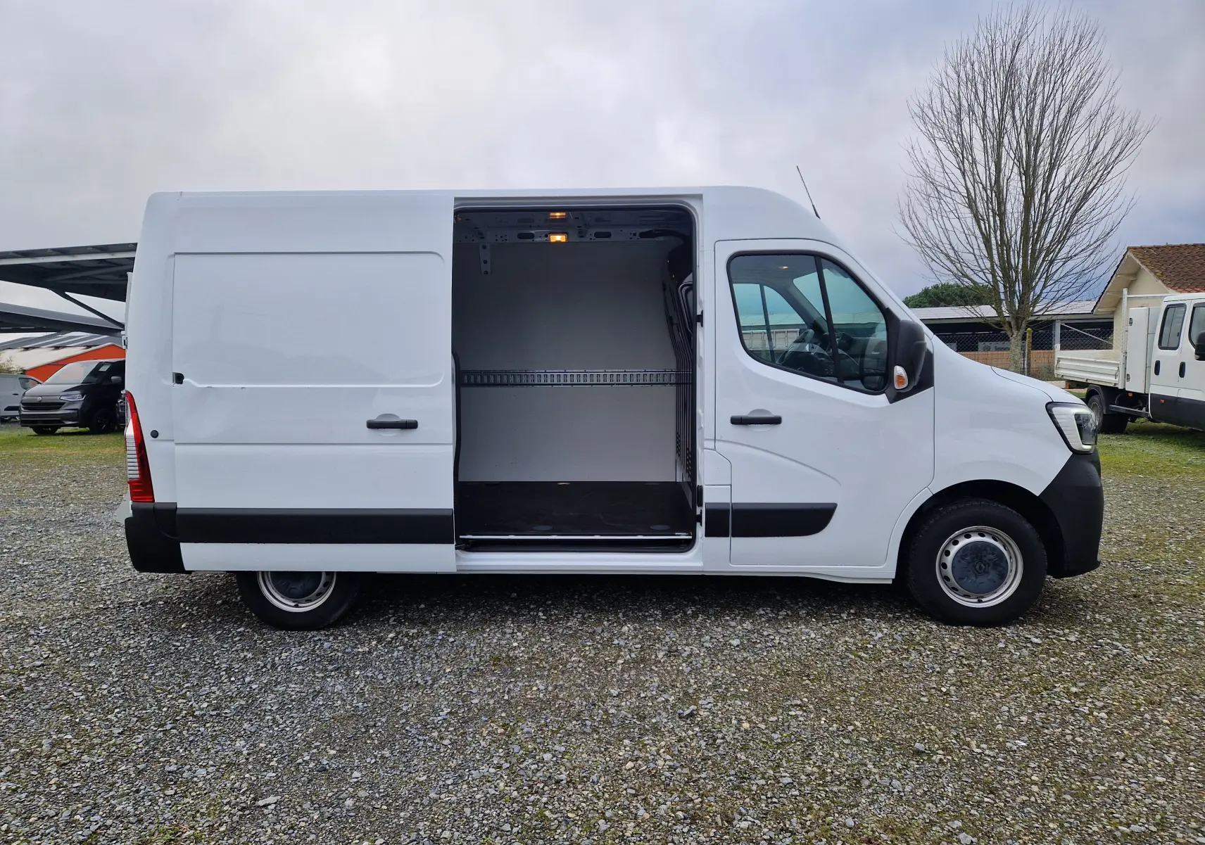 Vue latérale droite d'un Renault Master blanc 2023 avec porte coulissante ouverte dévoilant l'intérieur vide du fourgon.