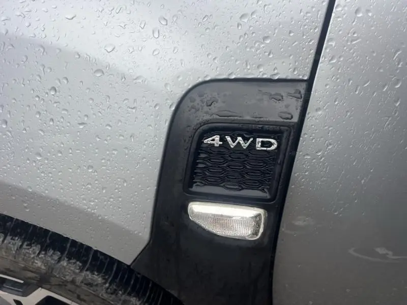Gros plan sur l'emblème 4WD noir et la carrosserie gris Comète métallisé du Dacia Duster 2021 côté avant gauche, avec gouttes d'eau.