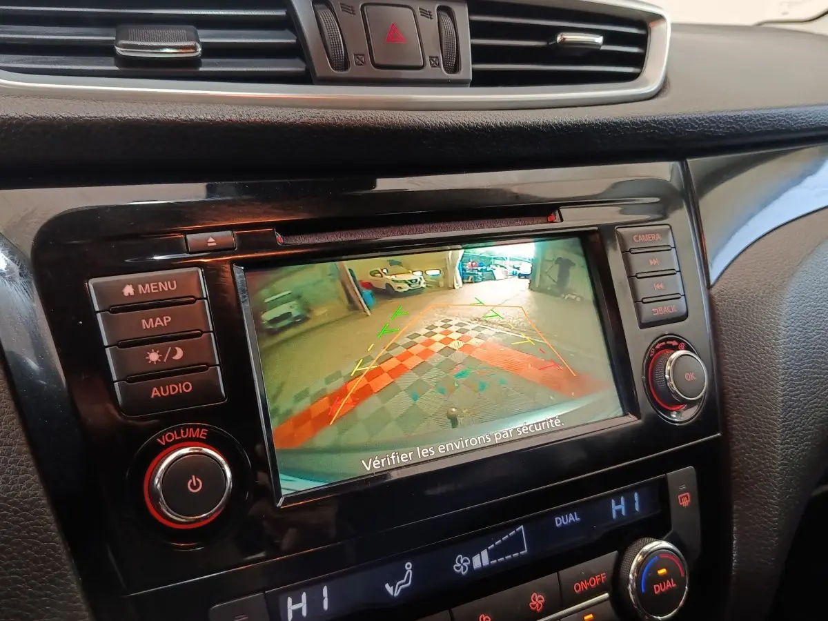 Vue rapprochée de l’écran tactile central noir du Nissan Qashqai gris clair, affichant la caméra de recul avec guidage coloré.