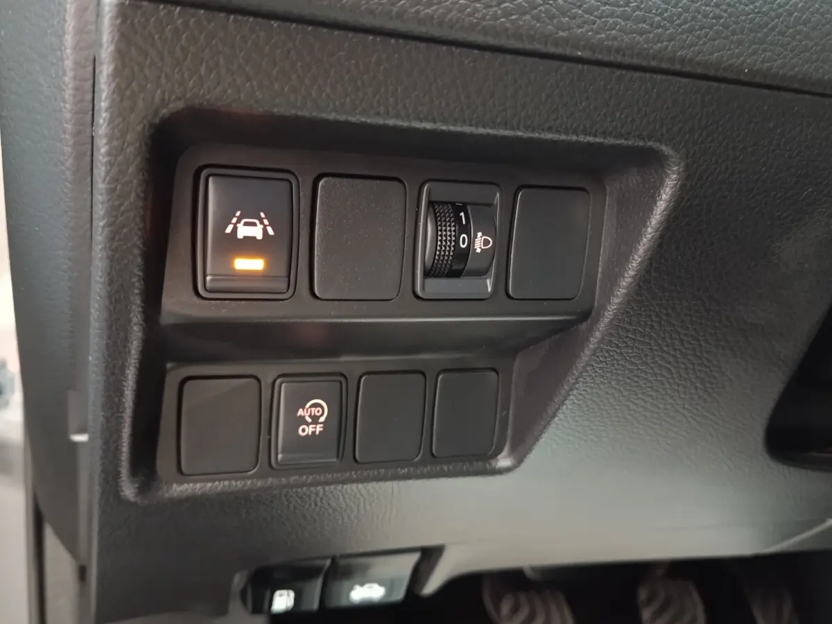 Gros plan sur les commandes du tableau de bord du Nissan Qashqai gris clair, avec boutons d’aide à la conduite allumés.