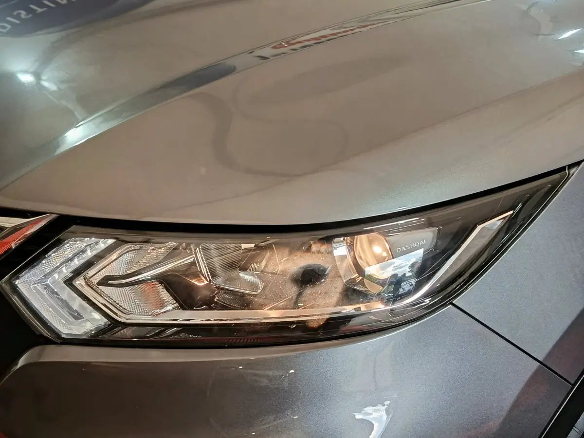 Gros plan sur le phare avant droit du Nissan Qashqai gris clair, mettant en valeur le design moderne et les détails lumineux.