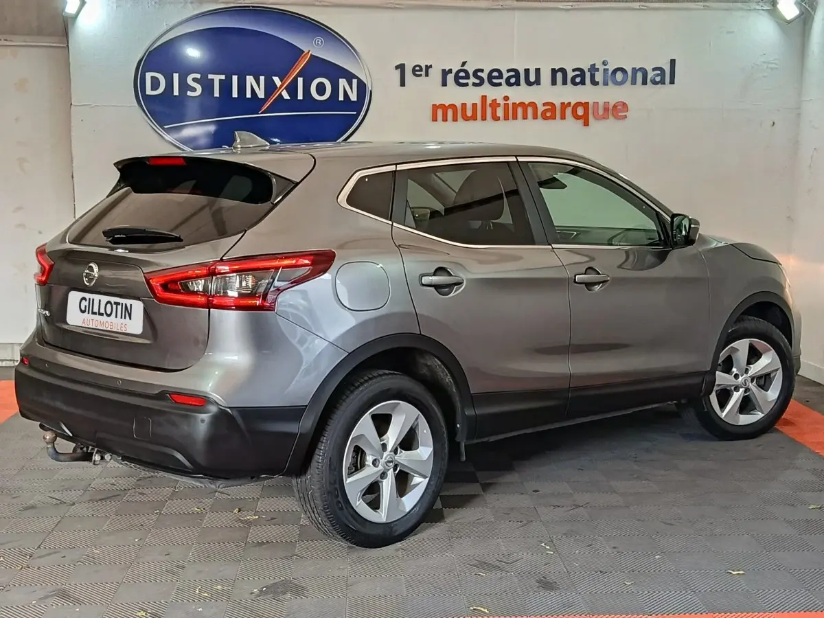 Vue 3/4 arrière droit d'un Nissan Qashqai gris clair garé en intérieur avec jantes alliage et feux arrière allongés.