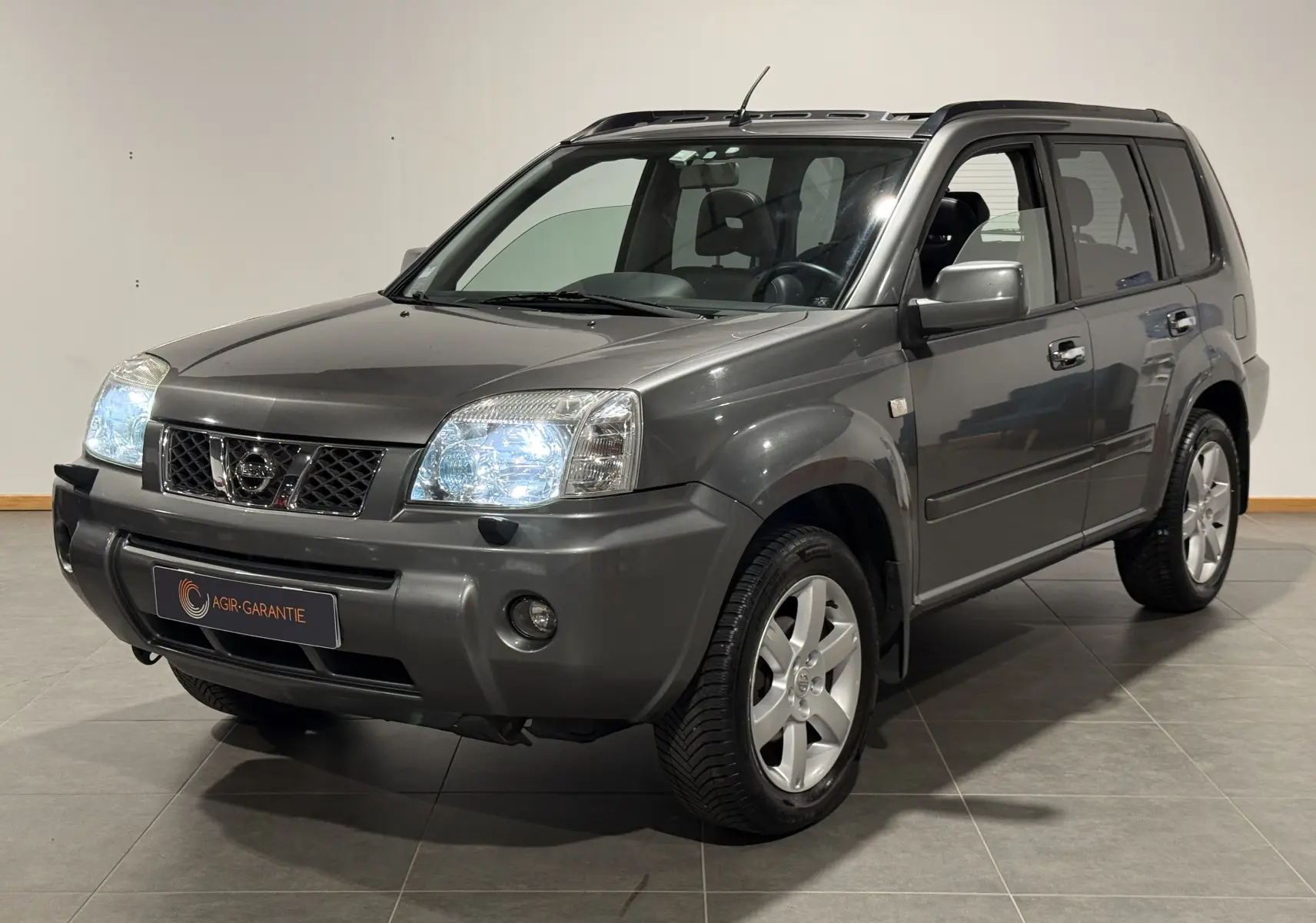Nissan X-TRAIL Columbia gris vue 3/4 avant droit avec phares allumés dans un intérieur neutre.