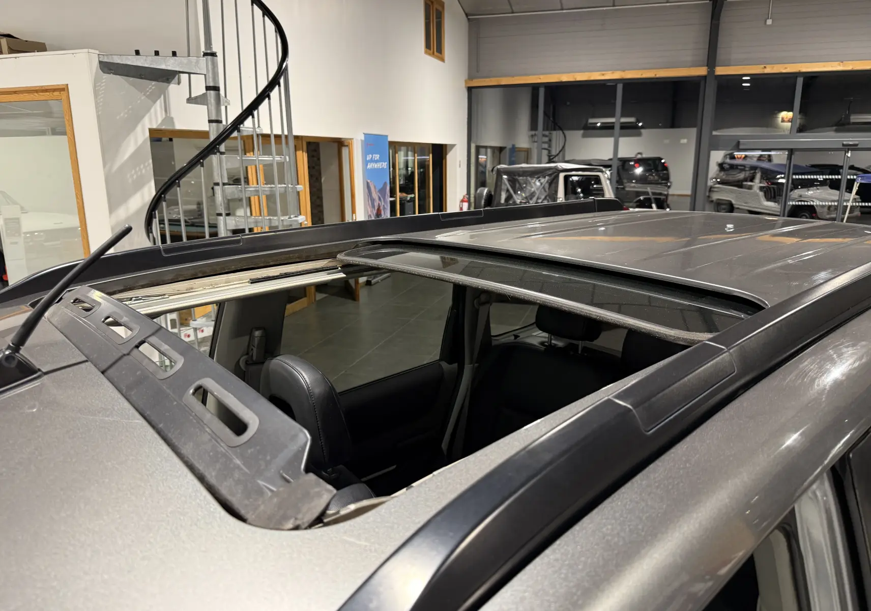 Toit ouvrant ouvert vu en plongée sur un Nissan X-TRAIL Columbia gris 2006 dans un showroom.