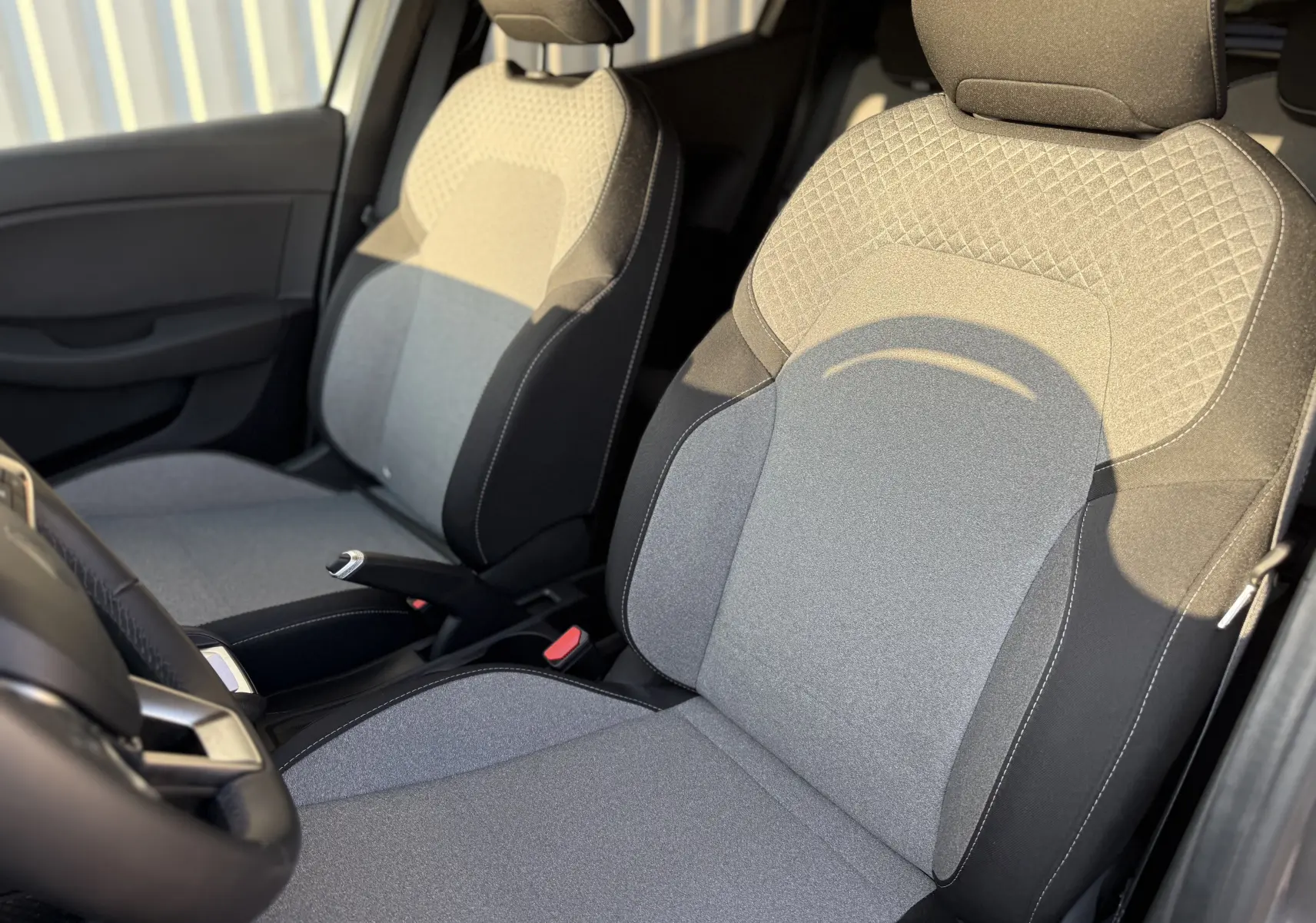 Gros plan sur les sièges avant en tissu gris clair et foncé de la Renault Clio V, intérieur lumineux côté conducteur.