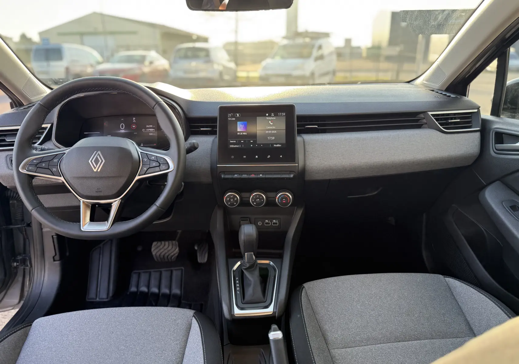 Vue intérieure avant de la Renault Clio V 2025, tableau de bord gris avec écran tactile et volant multifonction cuir.