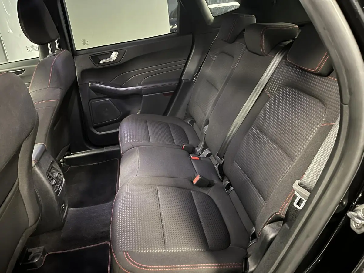 Vue intérieure arrière côté droit du Ford Kuga noir 2022, sièges tissu noir avec surpiqûres rouges et ceintures de sécurité visibles.