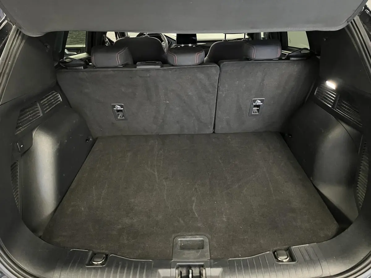 Coffre noir spacieux du Ford Kuga 2022 avec banquette arrière rabattue et éclairage intérieur allumé.