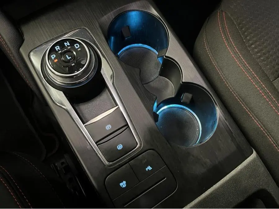 Vue rapprochée de la console centrale noire du Ford Kuga 2022 avec sélecteur rotatif et éclairage bleu des porte-gobelets.