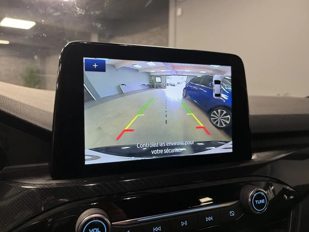 Écran central montrant la caméra de recul du Ford Kuga noir, avec vue arrière sur un parking intérieur.