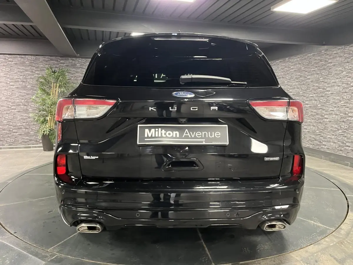 Vue arrière d'un Ford Kuga noir avec double sortie d'échappement et badges Hybrid et Kuga visibles.