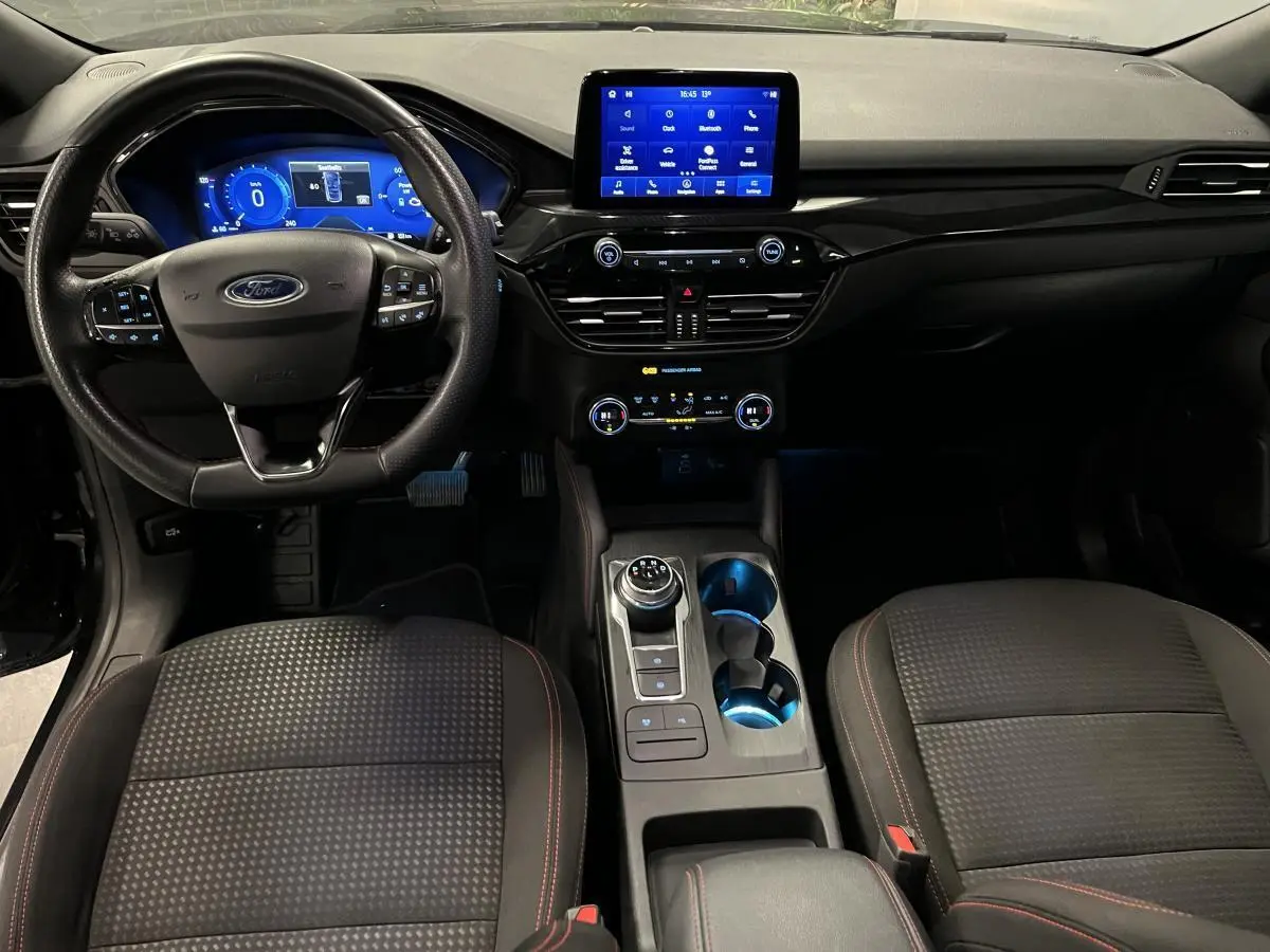 Vue intérieure avant du Ford Kuga noir 2022, tableau de bord numérique et console centrale avec sélecteur rotatif.