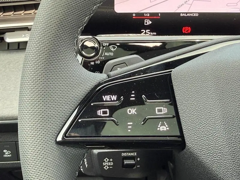 Gros plan sur les commandes au volant à gauche de l'Audi Q3 2026 noir Mythique, avec affichage digital en arrière-plan.