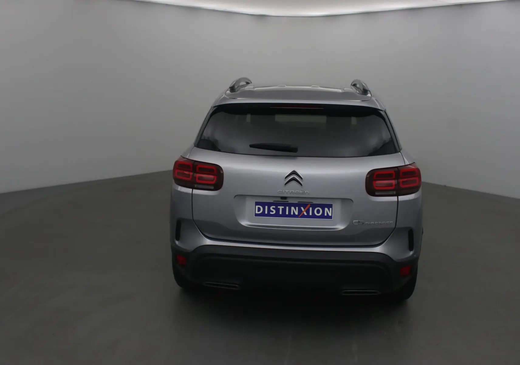 Vue arrière d'un Citroën C5 Aircross gris Artense avec feux arrière rouges et toit équipé de barres de toit.