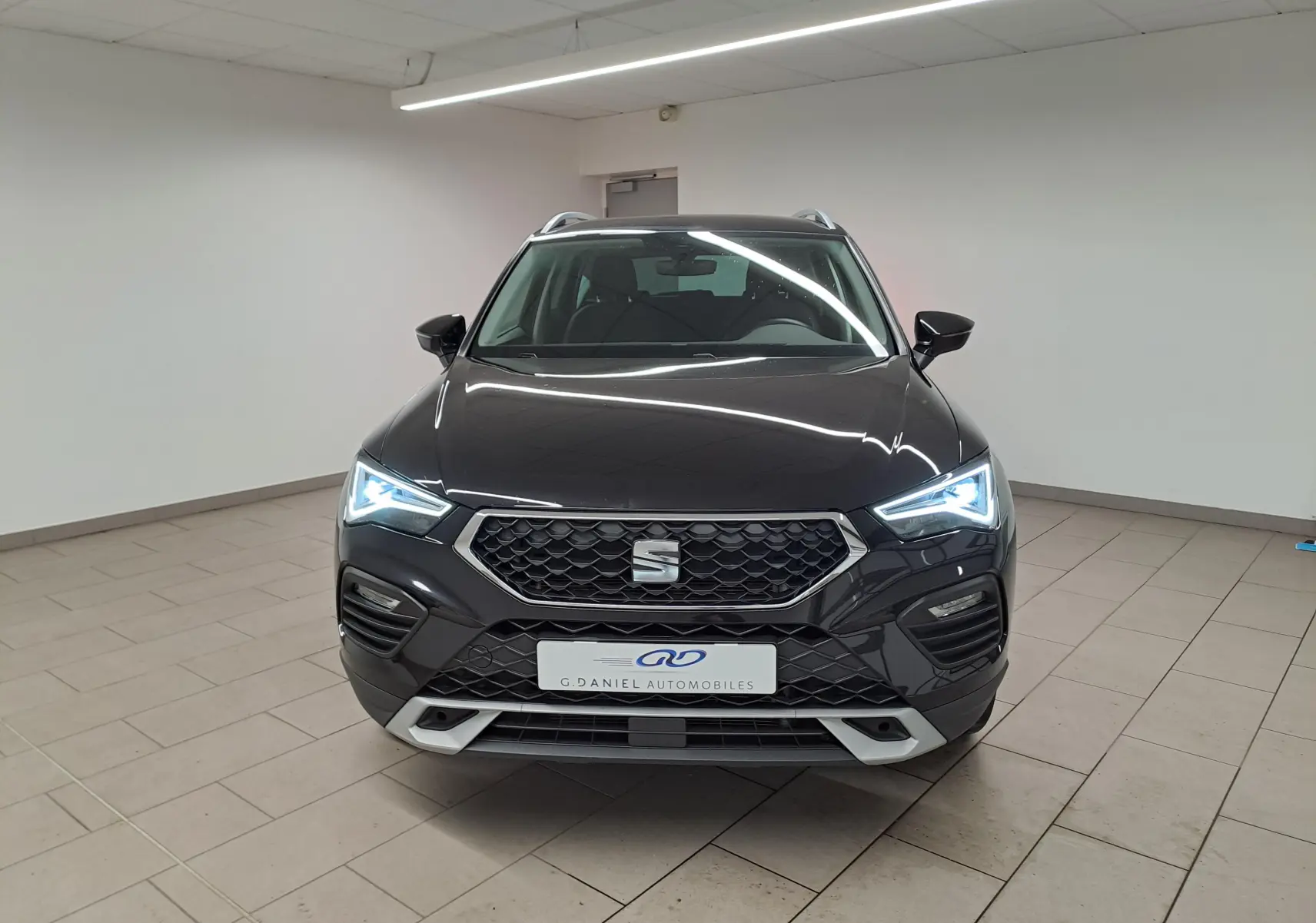 Vue frontale d'un SEAT Ateca 2023 noir minuit avec feux LED allumés dans un showroom intérieur.
