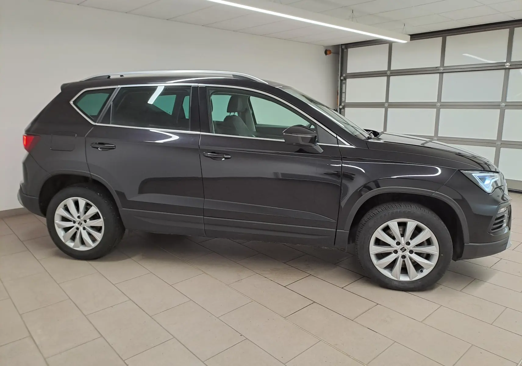 Vue de profil côté gauche d’un SEAT Ateca 2023 noir minuit avec jantes alliage et vitres teintées dans un garage.