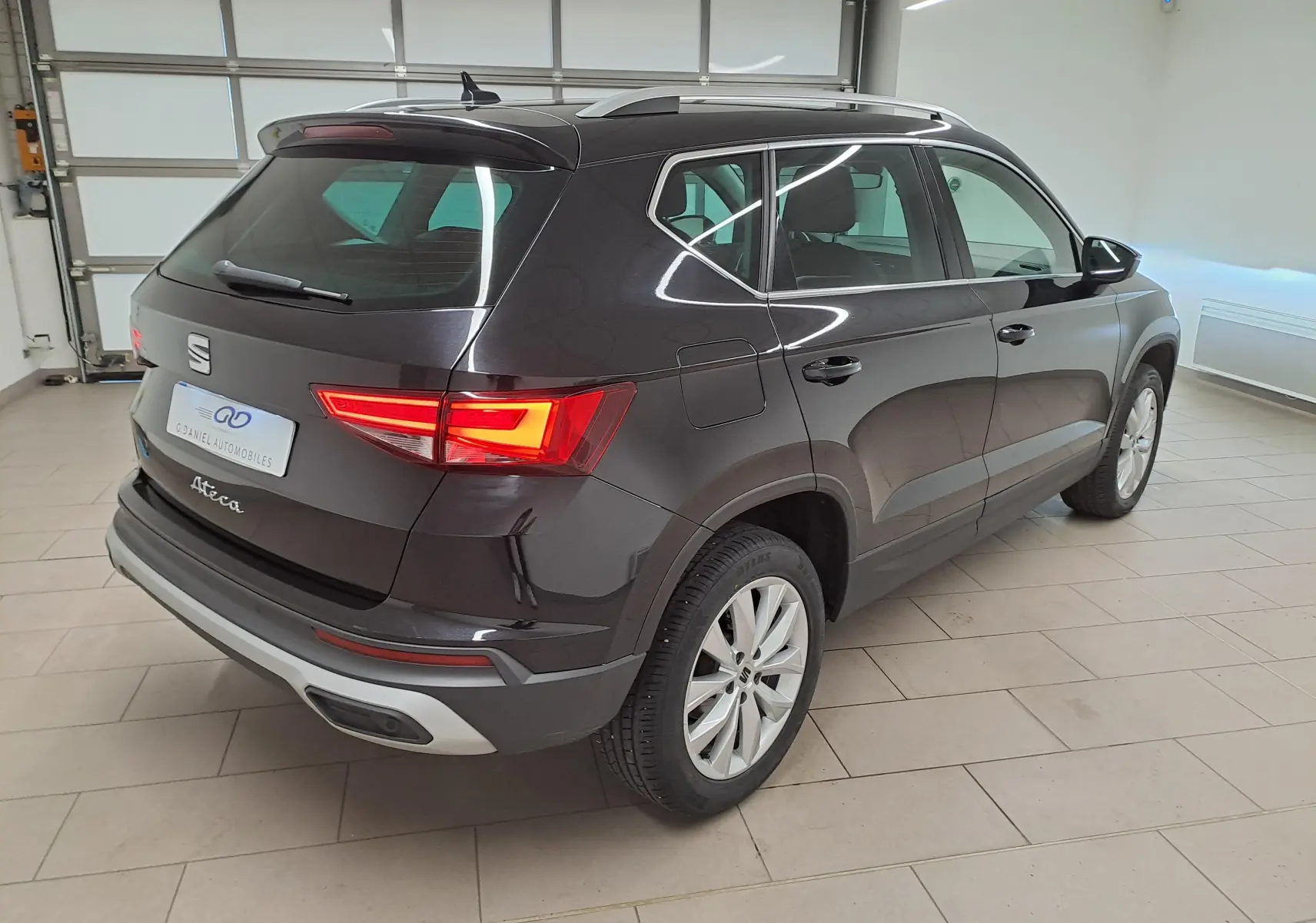 Vue 3/4 arrière droite d'un SEAT Ateca 2023 noir minuit avec feux arrière allumés dans un garage lumineux.