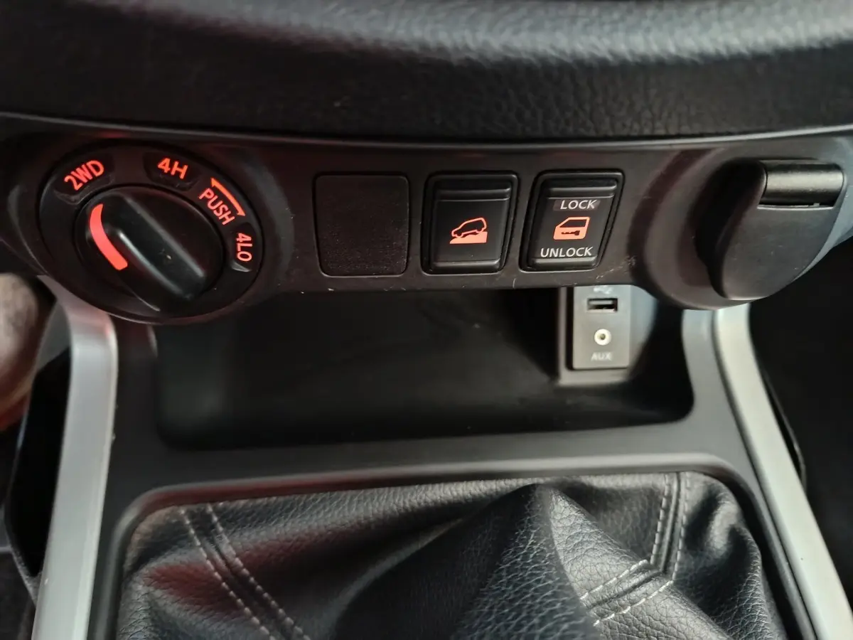 Gros plan sur la console centrale du Nissan Navara 2018, montrant les commandes de traction, verrouillage de benne et prise USB.