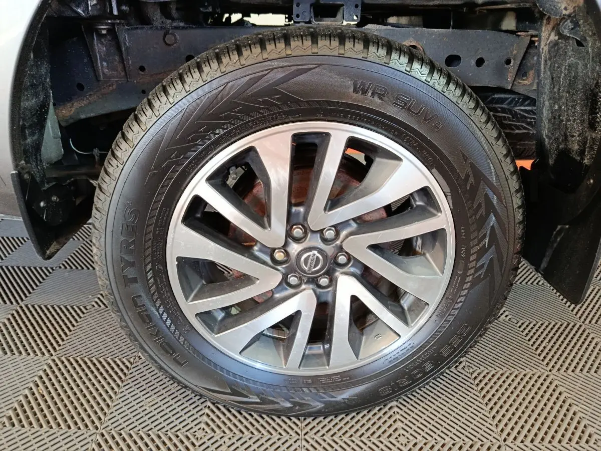 Gros plan sur la roue avant droite du Nissan Navara gris clair, jante alliage à plusieurs branches distinctives.