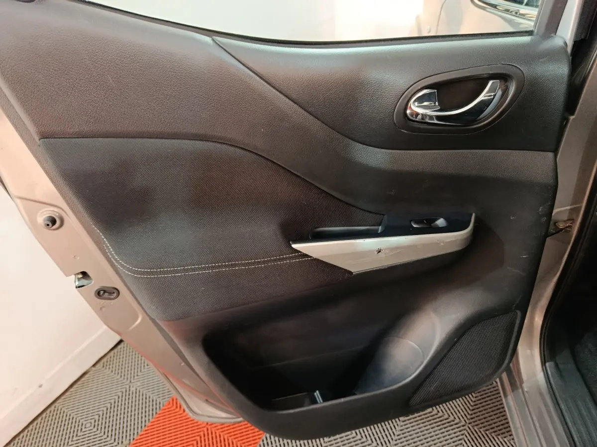 Vue intérieure de la porte avant gauche du Nissan Navara gris clair, avec poignée chrome et panneau noir texturé.