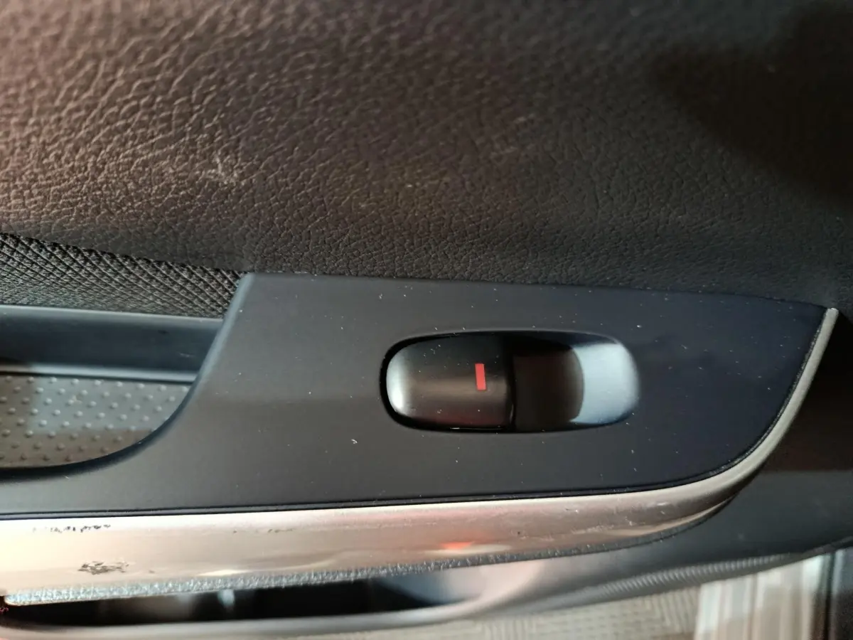 Gros plan sur le bouton de verrouillage central noir avec indicateur rouge, sur la porte intérieure d'un Nissan Navara gris clair.