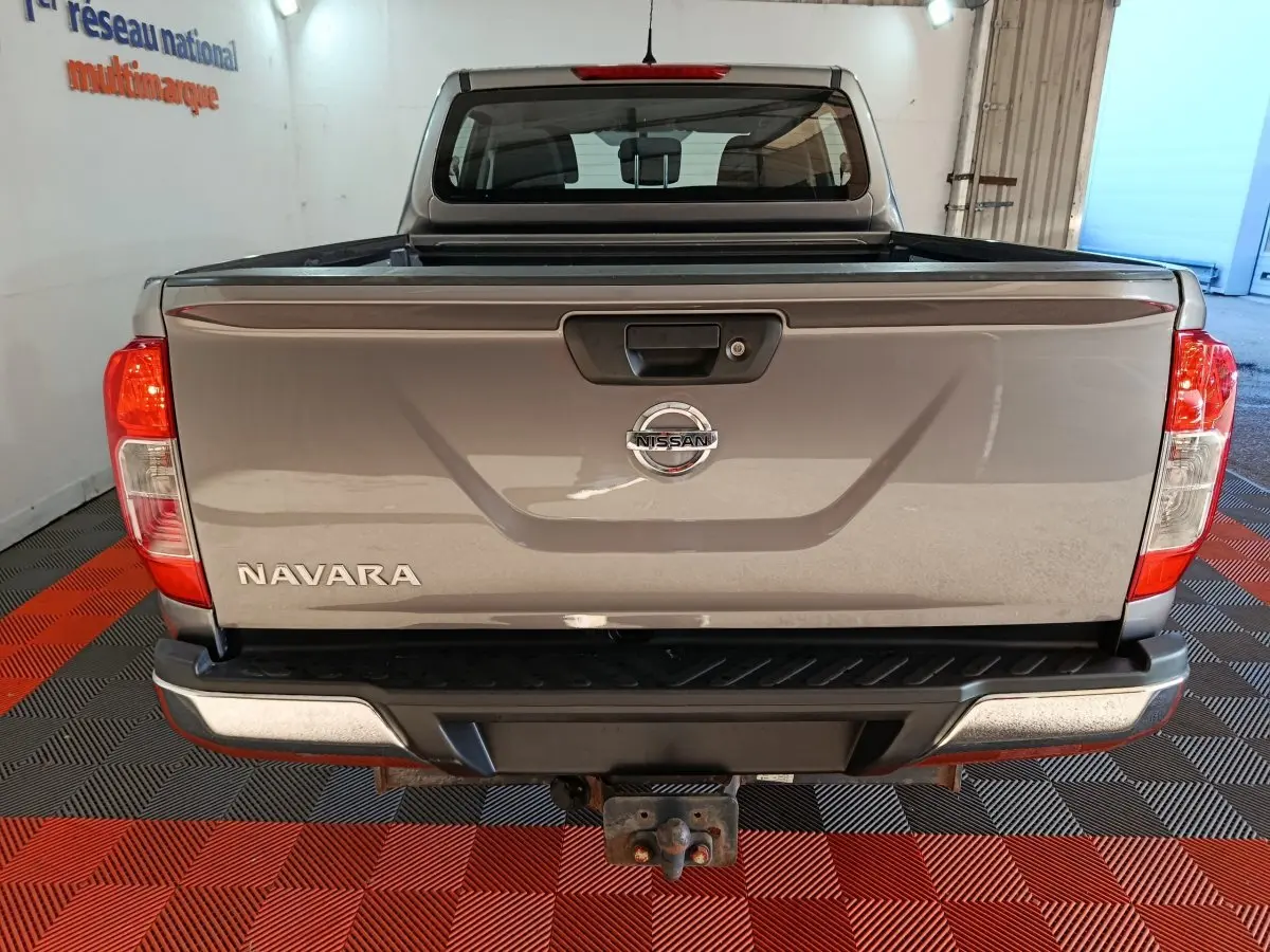 Vue arrière d’un Nissan Navara gris clair avec benne pick-up et attelage visible dans un garage.