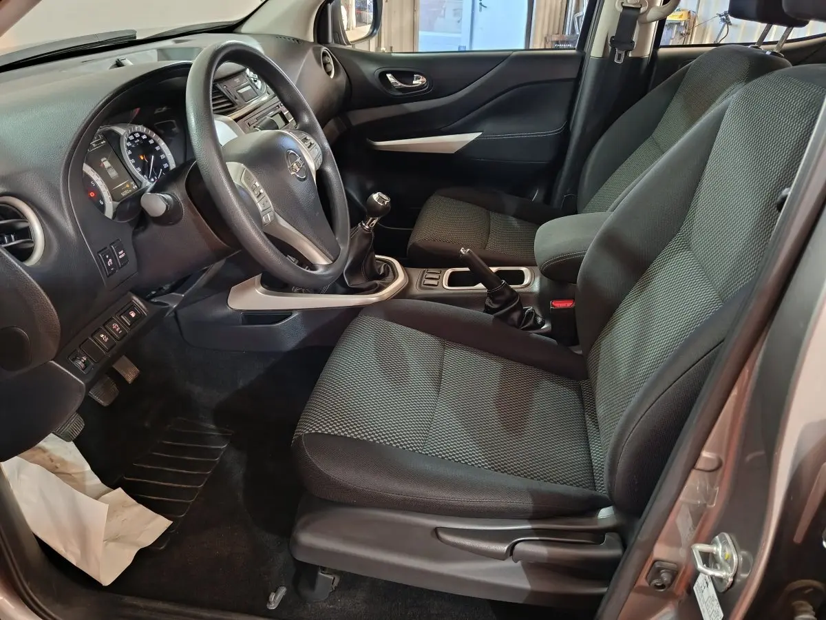 Vue intérieure côté conducteur du Nissan Navara gris clair 2018, montrant le volant multifonctions et la boîte manuelle.