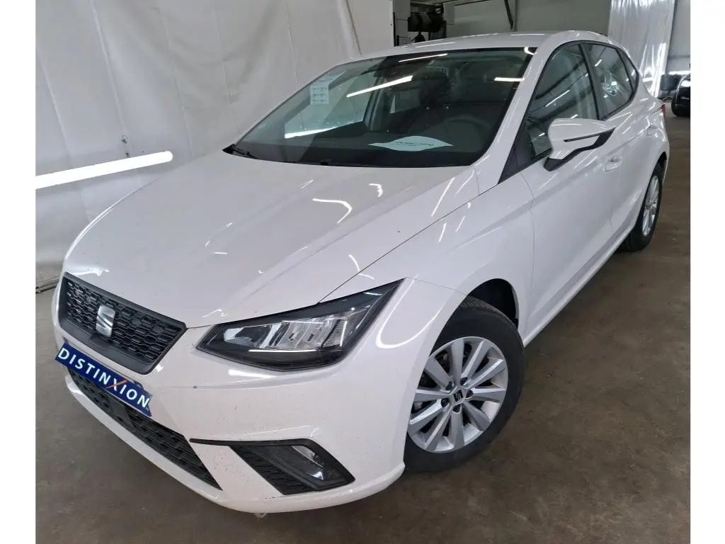 Vue 3/4 avant droite d'une SEAT Ibiza blanche 5 portes exposée en showroom avec jantes alliage et calandre noire.