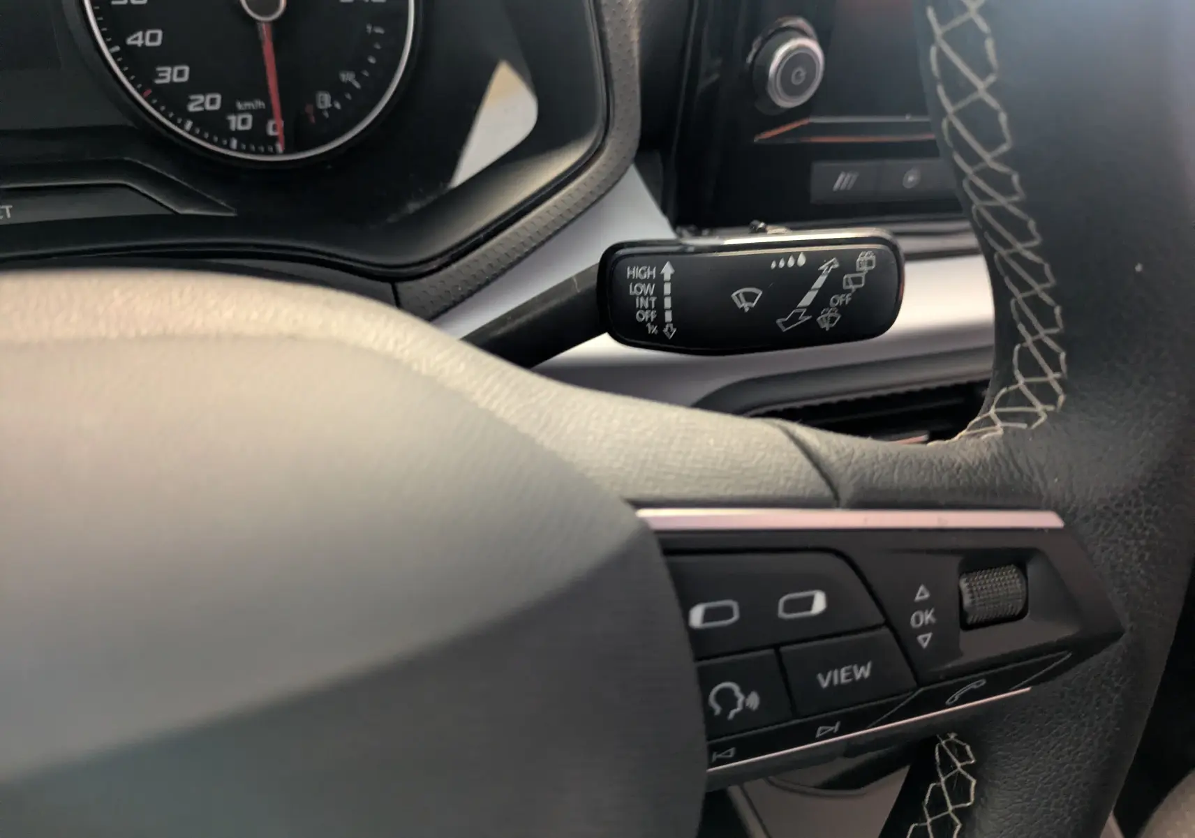 Gros plan sur le volant à droite avec commandes intégrées et levier d’essuie-glace, tableau de bord partiellement visible, intérieur noir.