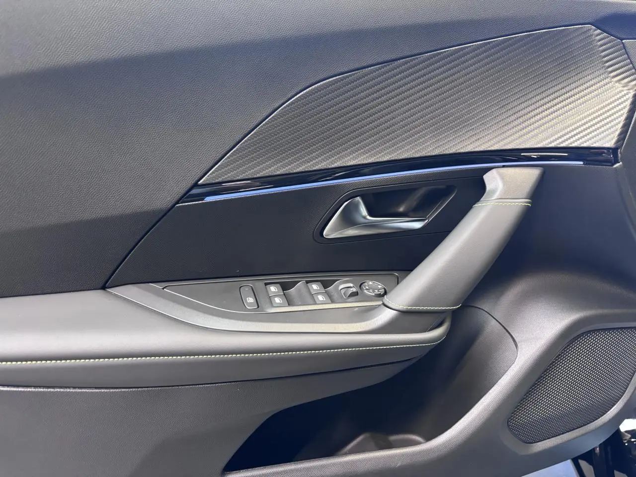 Détail de la porte avant gauche noire du Peugeot 2008 1.2i Hybrid 2026 avec surpiqûres vertes et insert carbone.